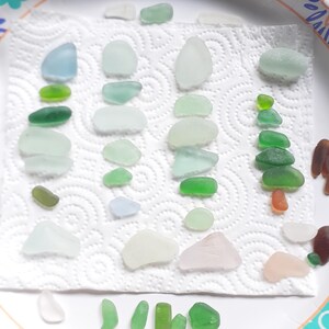 Puede incluir: Una colecci&oacute;n de piezas de vidrio de mar en varios tonos de verde, azul y blanco, dispuestas sobre una toalla de papel blanca. El vidrio de mar est&aacute; ordenado por color y tama&ntilde;o, con algunas piezas apiladas unas sobre otras.