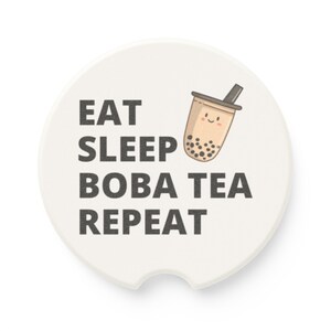 May include: White round coaster with black text that reads "Eat Sleep Boba Tea Repeat". A cartoon boba tea cup with a smiling face is above the text.