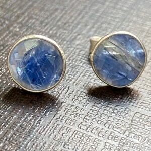 May include: A pair of silver earrings with blue gemstone cabochons. The gemstones have a shimmery, iridescent finish.