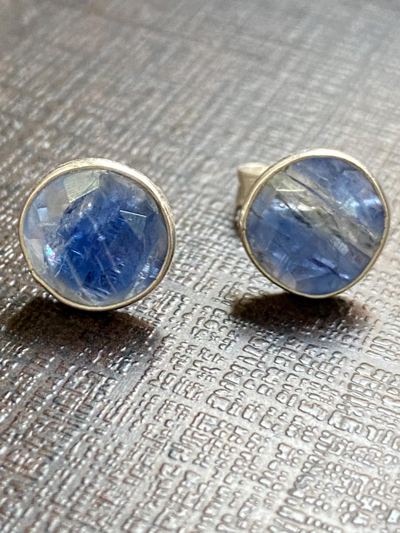 May include: A pair of silver earrings with blue gemstone cabochons. The gemstones have a shimmery, iridescent finish.