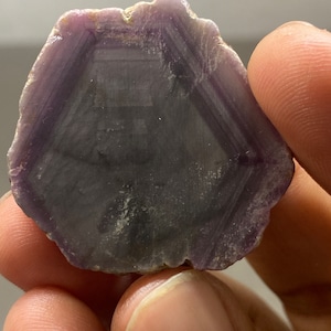 Puede incluir: Un cristal hexagonal de color morado y gris con un patrón en capas. El cristal es liso y pulido.