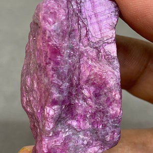 May include: A large, rough, purple ruby crystal with a deep, rich color. The crystal has a natural, unpolished surface.