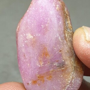 以下が含まれることがあります： ピンクのラフなジェムストーンで、不規則な形をしています。ジェムストーンはピンクの色合いで、茶色と白の模様があります。