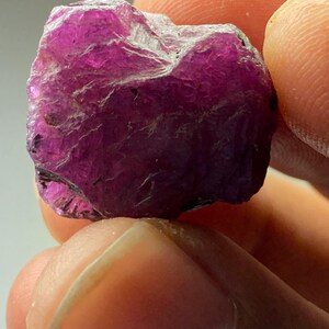 May include: A large, rough, purple gemstone with a deep, rich color. The gemstone has a natural, unpolished look and is a beautiful example of a raw crystal.