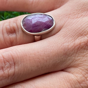 May include: A silver ring with a large, oval-shaped, faceted purple gemstone.