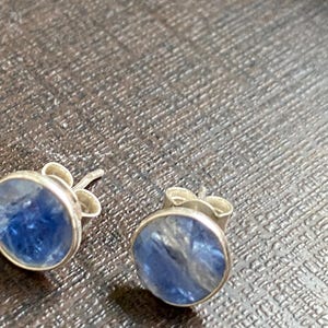 May include: A pair of silver stud earrings with blue gemstone accents. The gemstones have a shimmery, iridescent quality.