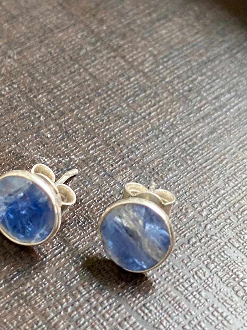 May include: A pair of silver stud earrings with blue gemstone accents. The gemstones have a shimmery, iridescent quality.