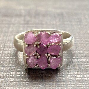 May include: A silver ring with a square-shaped setting filled with small, pink gemstones.