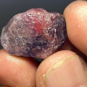 May include: A rough, purple and red gemstone with a natural, unpolished finish.