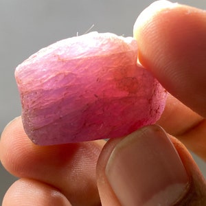 Puede incluir: Una gema rosa, facetada, de corte tosco, con una superficie estriada.