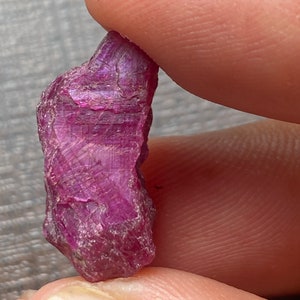 May include: A deep red ruby crystal with a rough, natural texture. The crystal is a vibrant shade of red and has a slightly translucent appearance.