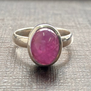 Può includere: Un anello d'argento con una pietra ovale rosa incastonata in una montatura a castone.