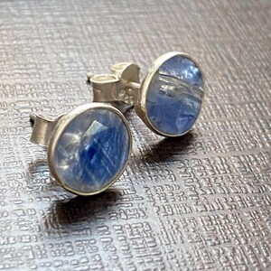 May include: A pair of silver stud earrings with blue gemstone accents. The gemstones have a cloudy, translucent appearance.