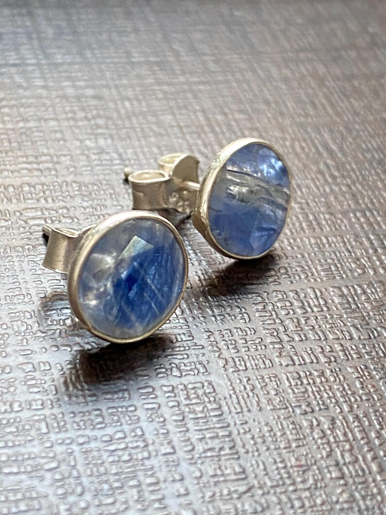 May include: A pair of silver stud earrings with blue gemstone accents. The gemstones have a cloudy, translucent appearance.