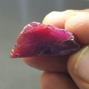 Puede incluir: Una piedra preciosa de rubí en bruto de color rojo intenso con forma triangular.