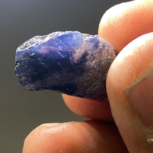 May include: A rough, purple and blue gemstone with a translucent appearance.
