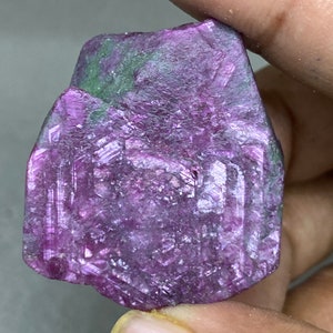 以下が含まれることがあります： 緑色のインクルージョンを含む、大きなファセットカットの紫色のルビーの結晶。結晶は、粗く自然な外観をしています。
