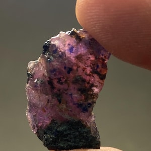 May include: A rough, purple and black crystal with a jagged edge. The crystal is translucent and has a dark, almost black, base.