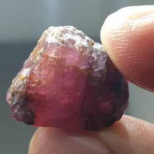 May include: A rough, pink and purple gemstone with a natural, unpolished finish.