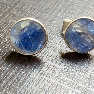 May include: A pair of silver earrings with blue gemstone cabochons. The gemstones have a shimmery, iridescent quality.