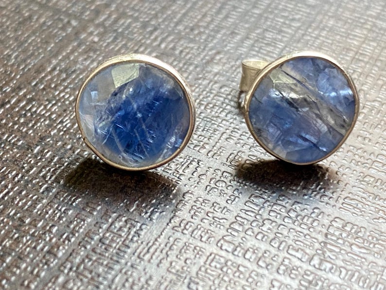 May include: A pair of silver earrings with blue gemstone cabochons. The gemstones have a shimmery, iridescent quality.