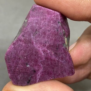 May include: A large, rough, purple ruby gemstone with a natural, irregular shape.