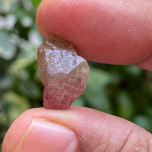 May include: A small, pink and brown, faceted crystal with a rough, natural texture.