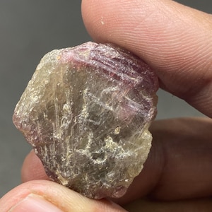 May include: A rough, translucent, pink and grey gemstone with a natural, irregular shape.
