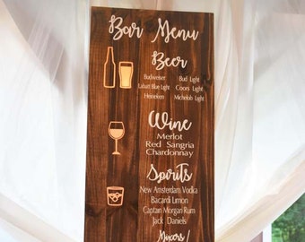 Pode incluir: Uma placa de madeira com uma mancha marrom, listando um menu de bar com opções de bebidas. A placa tem texto branco e ícones para cerveja, vinho, bebidas alcoólicas e misturas não alcoólicas. O texto inclui: "Bar Menu", "Beer", "Budweiser", "Bud Light", "Labatt Blue Light", "Coors Light", "Heineken", "Michelob Light", "Wine", "Merlot", "Red Sangria", "Chardonnay", "Spirits", "New Amsterdam Vodka", "Bacardi Limon", "Captain Morgan Rum", "Jack Daniels", "Mixers/Non-alcoholic", "Pepsi", "Diet Pepsi", "Mountain Dew", "Sprite", "Ginger Ale", "Orange Juice", "Cranberry Juice", "Cranberry Pineapple", "Seltzer", "Water".