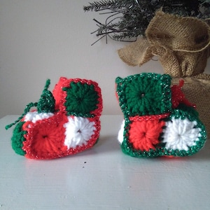 May include: A pair of crocheted baby booties in red, white, and green. The booties are made with a square pattern and have a festive Christmas theme.