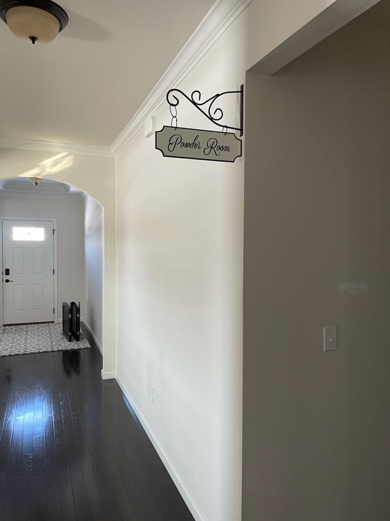 May include: A white hallway with dark wood floors and a sign that reads "Powder Room" hanging on the wall.
