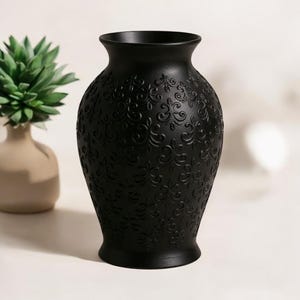 May include: A matte black vase with an embossed floral pattern. The vase has a wide base, a slender neck, and a flared rim. The vase is a decorative item for the home.