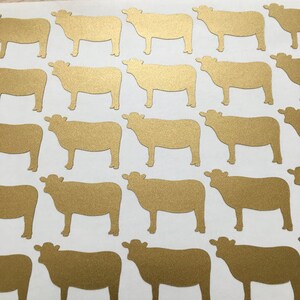 May include: A sheet of gold glitter cow stickers. The stickers are all the same size and shape, and they are arranged in a grid pattern.