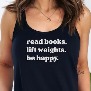 以下が含まれることがあります： 「read books. lift weights. be happy.」の白文字がプリントされた、ネイビーブルーのタンクトップ。丸首で細いストラップが付いています。画像は、人に着せられたタンクトップです。