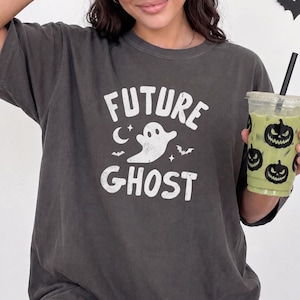 May include: A charcoal gray short-sleeve t-shirt featuring a white distressed graphic print that reads FUTURE GHOST, accompanied by a central ghost illustration, a crescent moon, small stars, and two small bats.