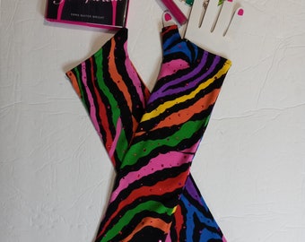 May include: A pair of long, fingerless gloves with a zebra stripe pattern in black, pink, red, orange, yellow, green, and purple. The gloves are embellished with small, pink rhinestones. A book titled "Schiaparelli" and a colorful beaded necklace are also visible.