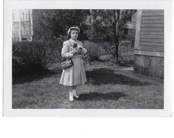Easter Sunday. Vintage snapshot photo of a well-dressed girl holding a pet puppy.