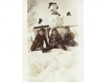 Winter fun! Undated vintage snapshot of children sitting at the base of a snowman.