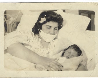 New Mother. Vintage photo of a woman wearing a mask and holding her baby in a hospital bed.