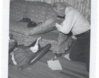 Where is it? 1960s vintage snapshot of a girl and an older man searching a couch.