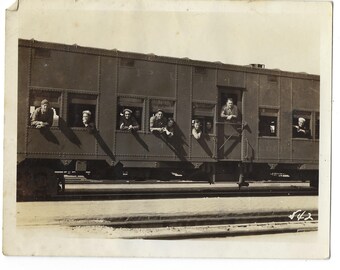 Transporting men in uniform. Undated vintage photo of a sailor and soldiers leaning out the window of a train&#39;s cattle car.