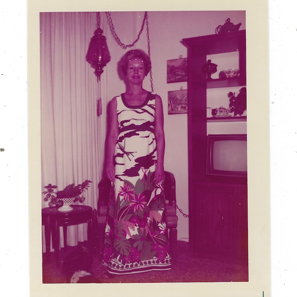 Fashions of 1976: Vintage snapshot of a woman posed in a bold nature/floral print dress in front of a tv console.