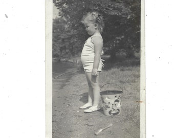 Perplexed. Undated vintage snapshot of a little girl with her bucket and shovel.