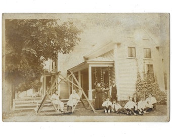 The girls get the glider boys on the ground. Faded RPPC of a large family posed in front of a suburban home.