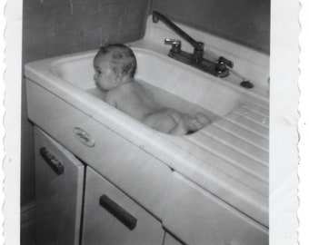 Bath time! Undated vintage snapshot of a baby in a kitchen sink.