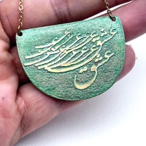 Pode incluir: Um colar verde e dourado com um pingente semicircular que apresenta caligrafia árabe intrincada. O pingente é feito de metal e tem uma superfície texturizada.