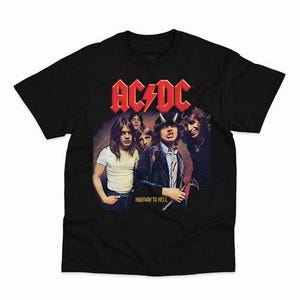 Puede incluir: Una camiseta negra de manga corta con un estampado gráfico de la banda AC/DC. El diseño incluye el logotipo rojo de AC/DC en la parte superior, una fotografía de los miembros de la banda y el texto HIGHWAY TO HELL impreso en amarillo.