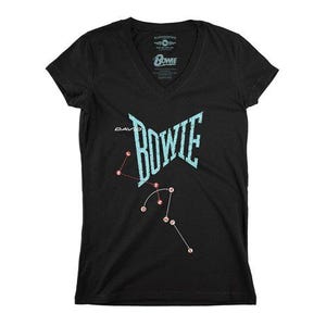 May include: A black V-neck t-shirt featuring a light blue distressed graphic of the text David Bowie. Below the name, a constellation-style diagram connects red circular dots labelled with the letters L, E, T, S, D, A, N, C, E in white.