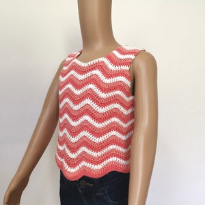 Op de afbeelding: Een mouwloos gehaakt topje met een golvend roze en wit gestreept patroon. Het topje is gecropped en heeft een gegolfde zoom.