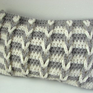 May include: A gray and white crocheted pillow with a cable knit pattern. The pillow is rectangular and has a soft, textured surface.